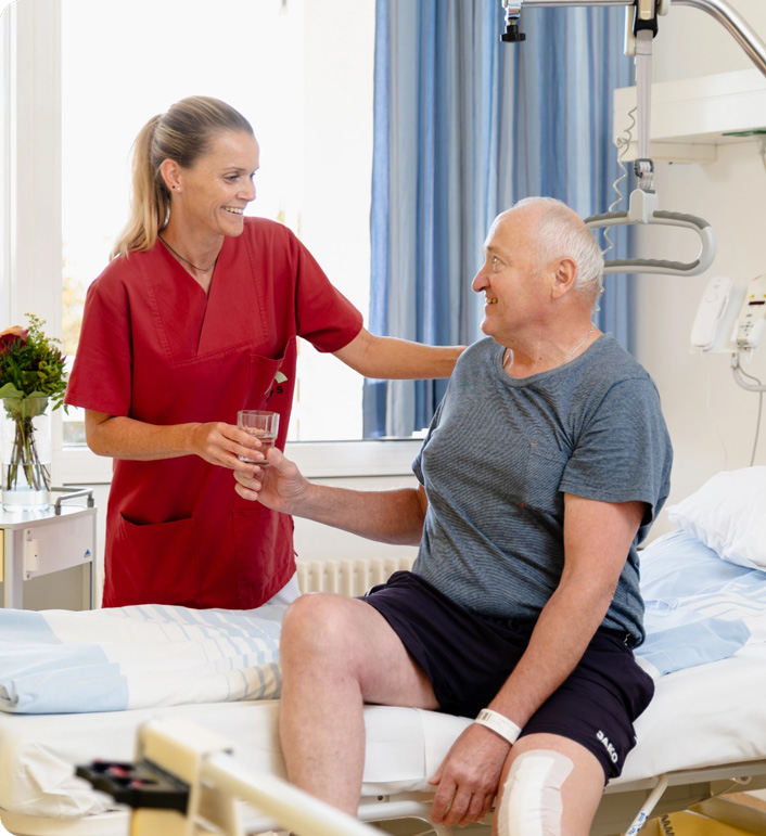 Patient sitzt im Bett und bekommt von der Krankenschwester ein Glas Wasser gereicht